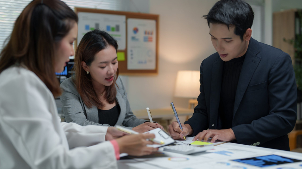 Asian businesspeople working together in the office, analyzing financial charts, discussing strategies, and taking notes during a productive meeting